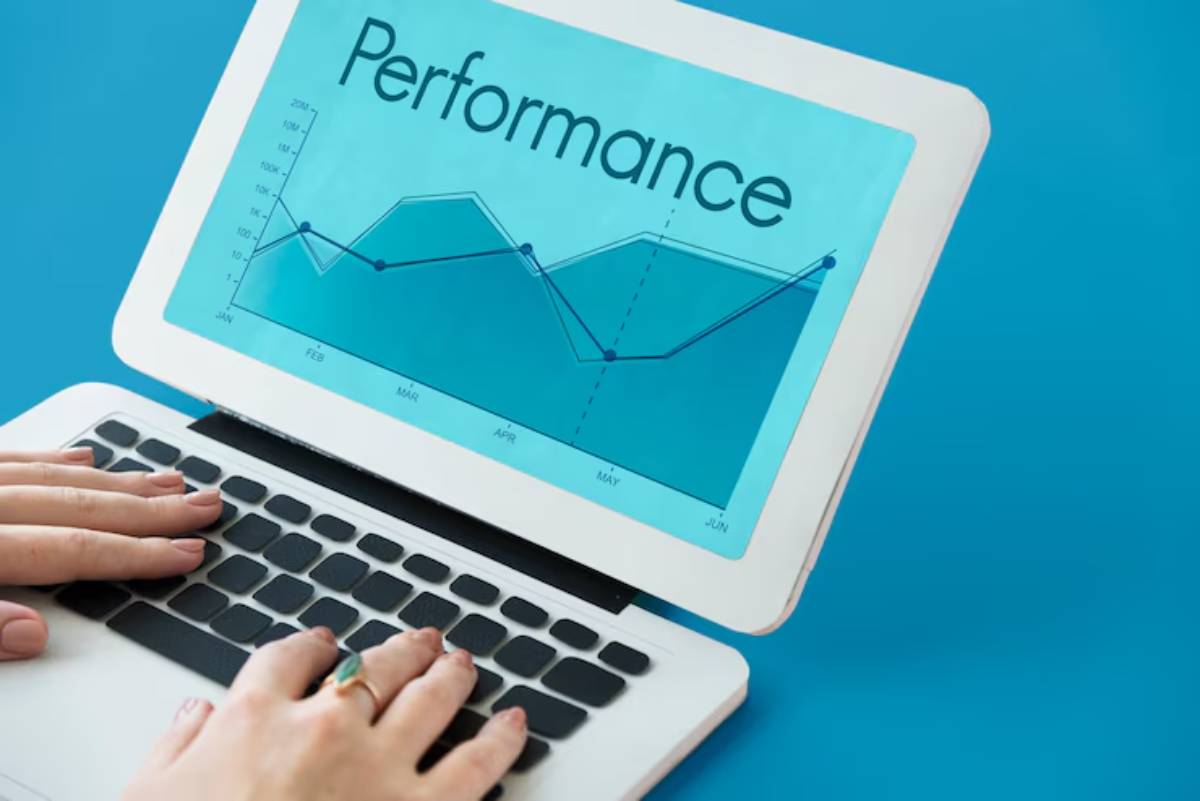 A person’s hands typing on a laptop, displaying a performance chart with monthly data trends on a bright blue background.