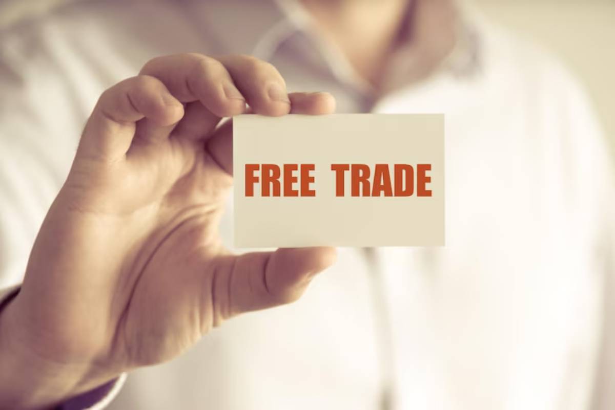 A person in a white shirt holds a business card displaying the phrase FREE TRADE in bold, red letters.