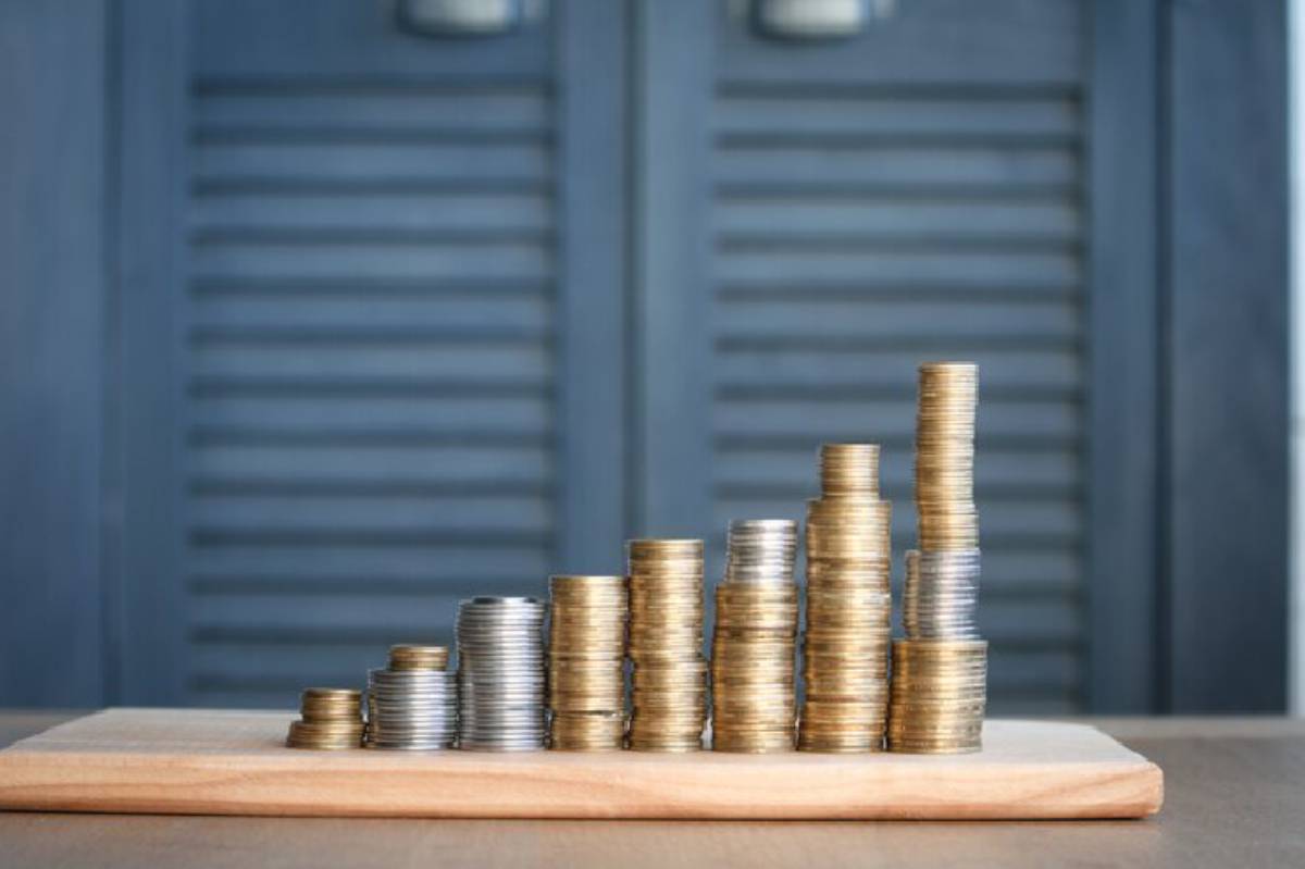 A wooden board displays stacked coins in varying heights, creating a bar graph effect against a blue background.