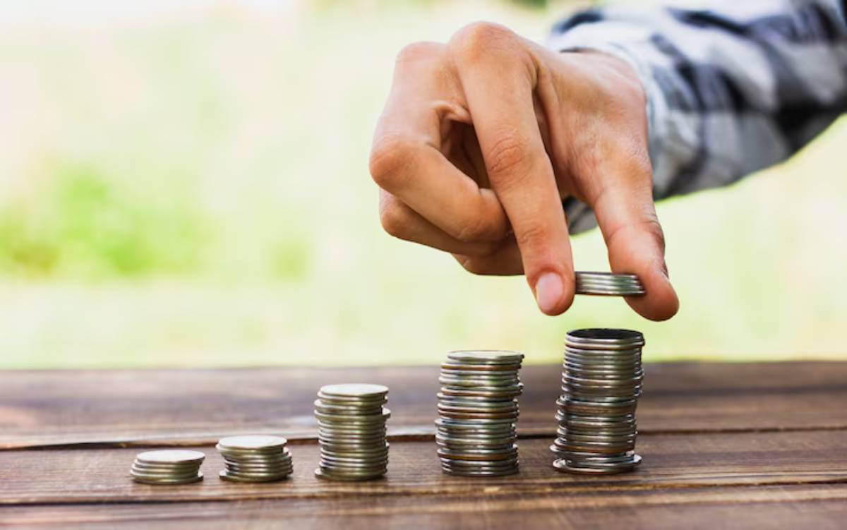 A hand stacking coins into ascending piles on a wooden table, symbolizing saving or investment growth.