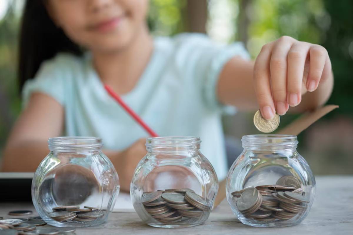 A young girl places a coin into one of three jars filled with coins, illustrating the concept of saving money.