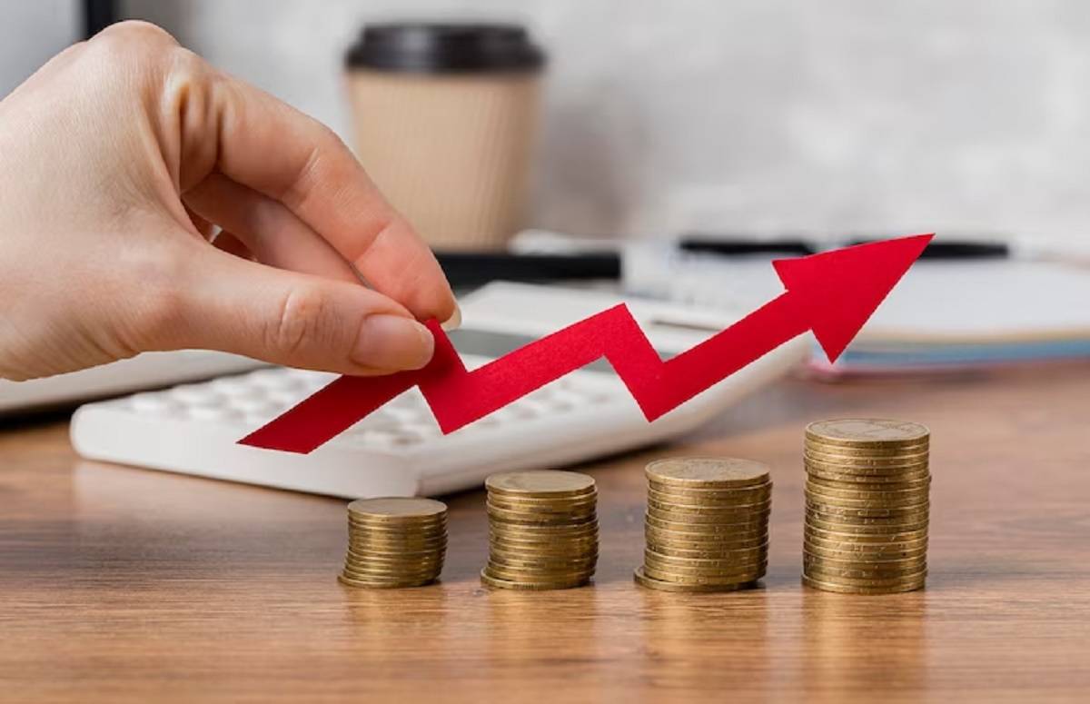 A hand places a red arrow graph above stacked coins, symbolizing financial growth and investment success on a wooden desk.