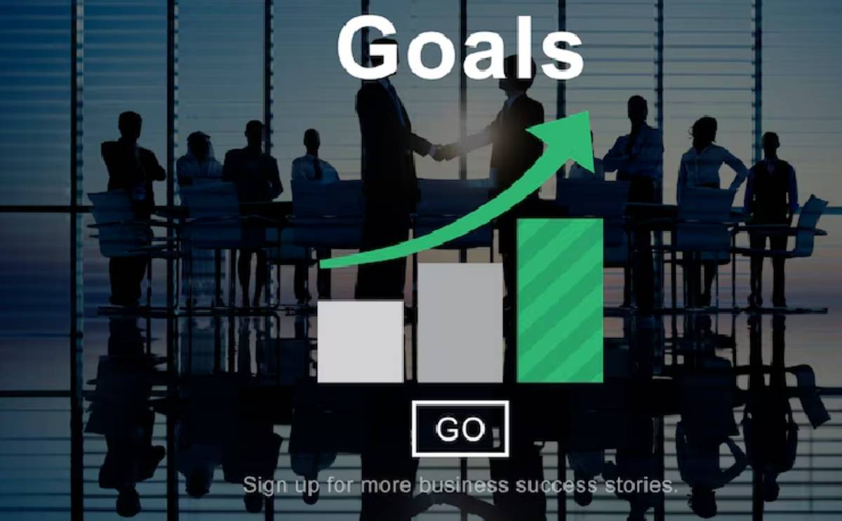Silhouettes of business professionals shaking hands with an upward trending graph labeled Goals in front of a conference room.
