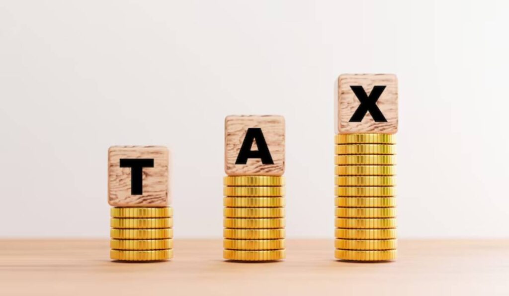 Stacks of gold coins rising, each topped by wooden blocks spelling TAX representing the concept of taxes.