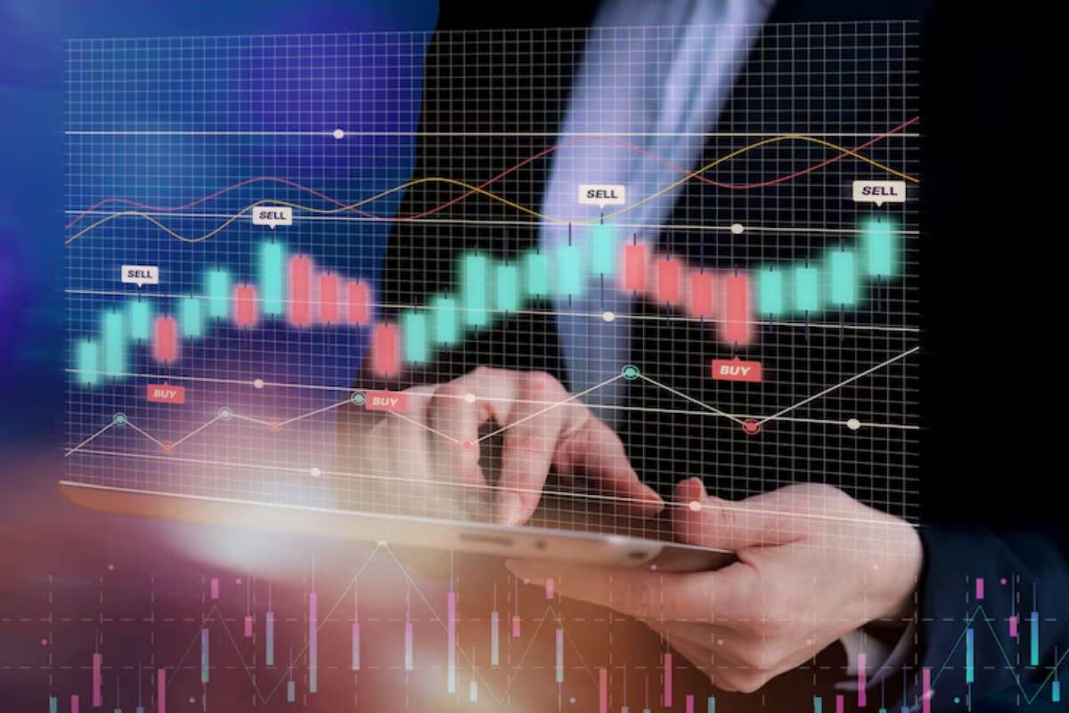 A person in a suit interacts with a tablet displaying financial charts with buy/sell indicators and colorful candlestick graphs.