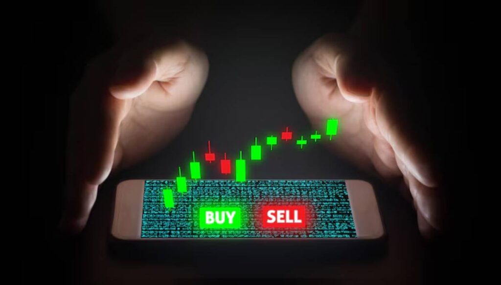 A smartphone displays a green button, with a rising candlestick chart, hands hovering protectively above it.