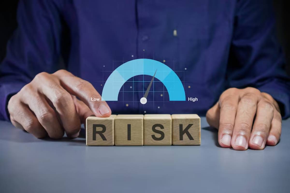 A person adjusts a risk gauge, with wooden blocks spelling RISK in front, emphasizing risk assessment in a business context.