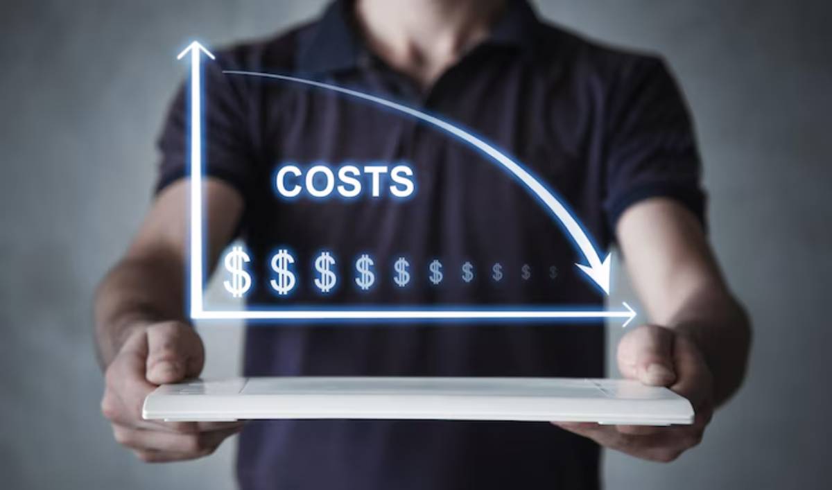 A person holds a tablet displaying a graph indicating decreasing costs, with the word COSTS prominently featured.