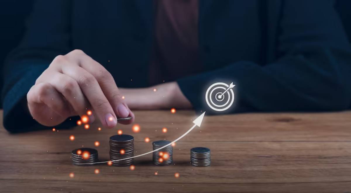 A hand stacking coins with a graphical arrow and target symbol, representing financial growth and investment goals.