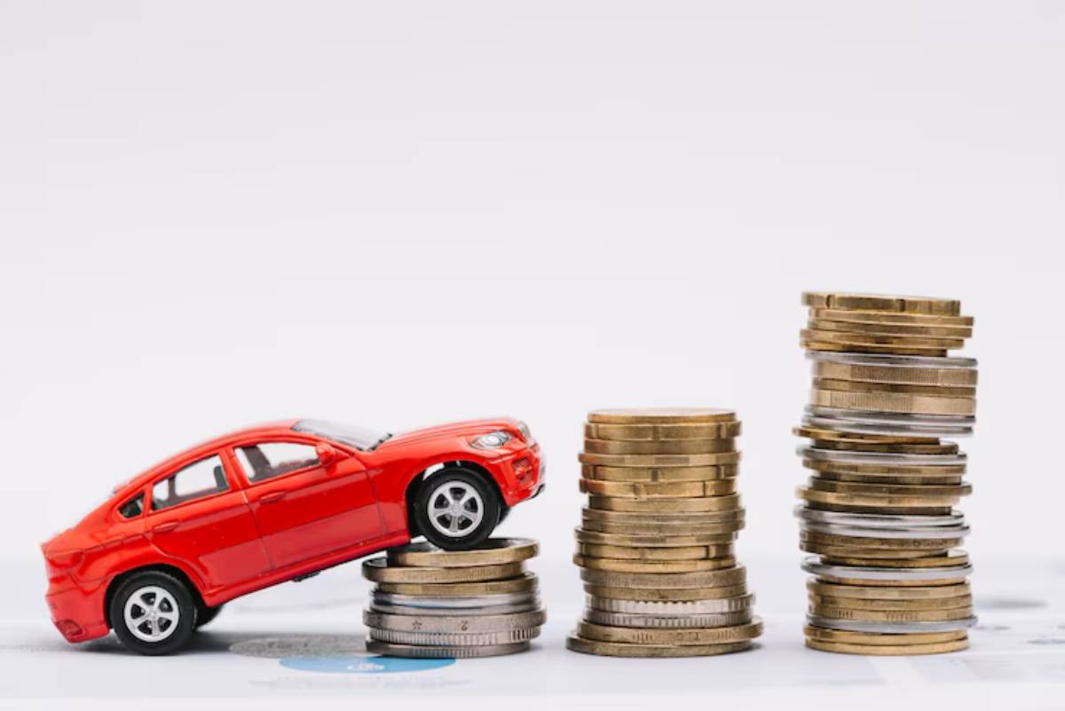 A red toy car balances on stacked coins, representing financial growth or investment.