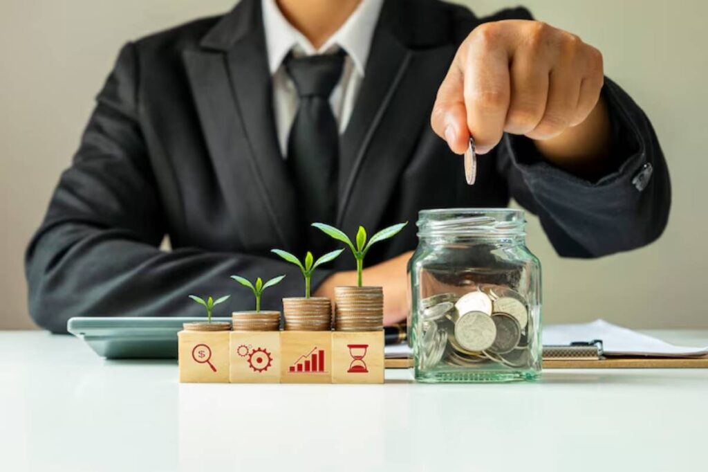 A businessman in a suit drops a coin into a jar surrounded by stacked coins and small plant sprouts, symbolizing investment growth.