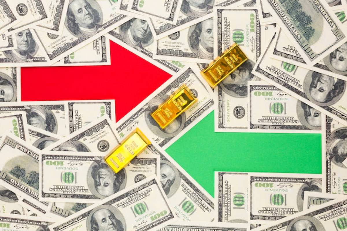 A background of scattered hundred-dollar bills with red and green arrows and gold bars placed between them.